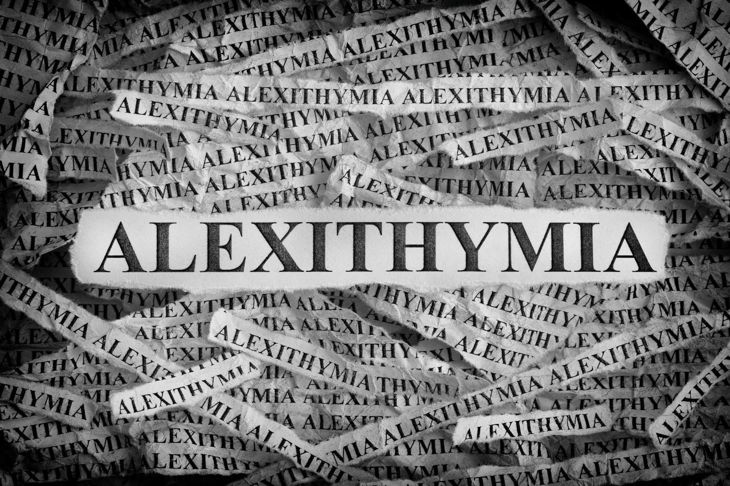 The image features the word 'ALEXITHYMIA' prominently displayed in large, bold letters across the center. Surrounding this central text are numerous smaller, repeated instances of the word 'ALEXITHYMIA' on torn strips of paper, creating a layered and chaotic background. The overall color scheme is monochromatic, with shades of black, white, and gray, giving the image a dramatic and intense appearance.
