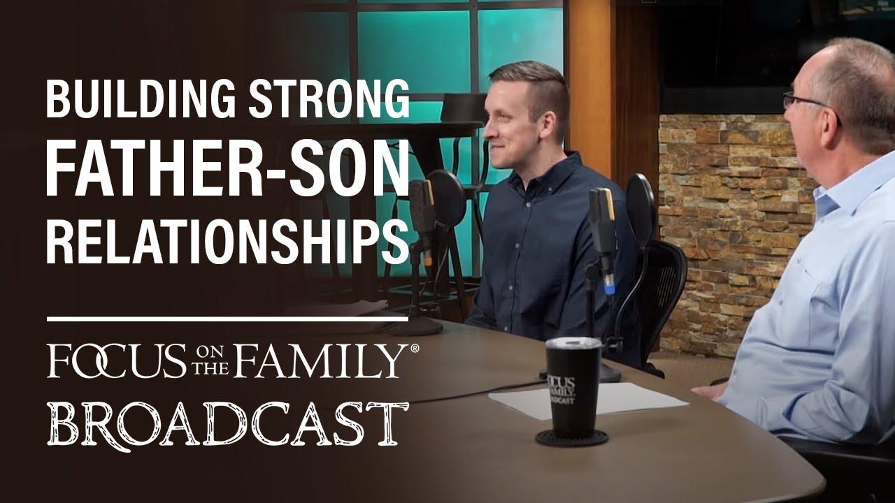 The image shows a broadcast setting with two men seated at a table, engaged in conversation. They are in a studio environment with microphones in front of them. The background features a stone wall and a window with a teal tint. On the left side of the image, there is text that reads 'BUILDING STRONG FATHER-SON RELATIONSHIPS' and 'FOCUS ON THE FAMILY BROADCAST'. A coffee cup with the 'FOCUS ON THE FAMILY' logo is visible on the table.