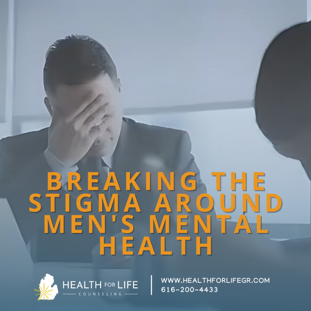 The image features a man in a suit sitting at a table with his hand covering his face, suggesting a moment of stress or contemplation. The background is a light, neutral color, and another person is partially visible on the right side of the image. Overlaid on the image is bold, orange text that reads 'BREAKING THE STIGMA AROUND MEN'S MENTAL HEALTH.' Below this, there is a logo and text for 'HEALTH FOR LIFE COUNSELING' along with a website URL 'WWW.HEALTHFORLIFEGR.COM' and a phone number '616-200-4433.' The overall theme of the image is focused on addressing and reducing the stigma associated with men's mental health issues.