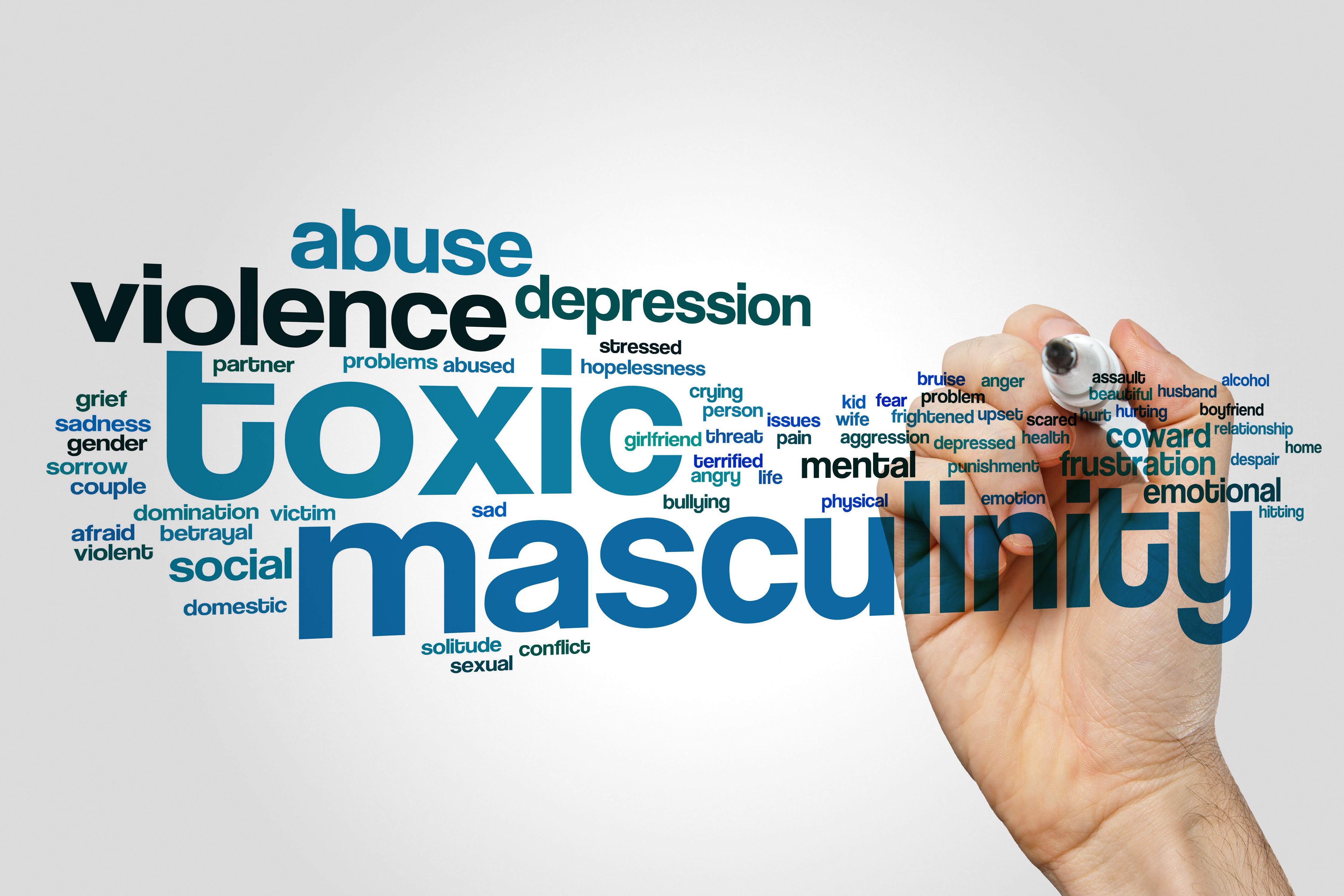 The image is a word cloud centered around the theme of 'toxic masculinity.' The largest words are 'toxic' and 'masculinity,' indicating the main focus. Surrounding these are various related terms such as 'violence,' 'abuse,' 'depression,' 'coward,' 'frustration,' 'emotional,' 'social,' 'mental,' and 'aggression.' The words are in different shades of blue and black, with varying sizes to emphasize their relevance. A hand is visible on the right side, holding a marker, suggesting the words are being written or highlighted. The background is a plain, light gray, which helps the words stand out.